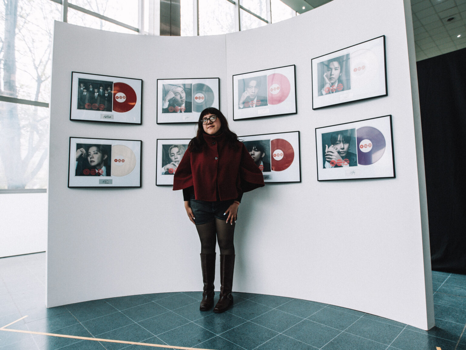 A visitor posing in front of the framed single covers at the BTS POP-UP: ARIRANG IN BUENOS AIRES, Centro de Convenciones Dr. Arturo Frondizi, Vicente Lopez, 2026 — photographed by Anita Almaraz for K-HipHop Argentina