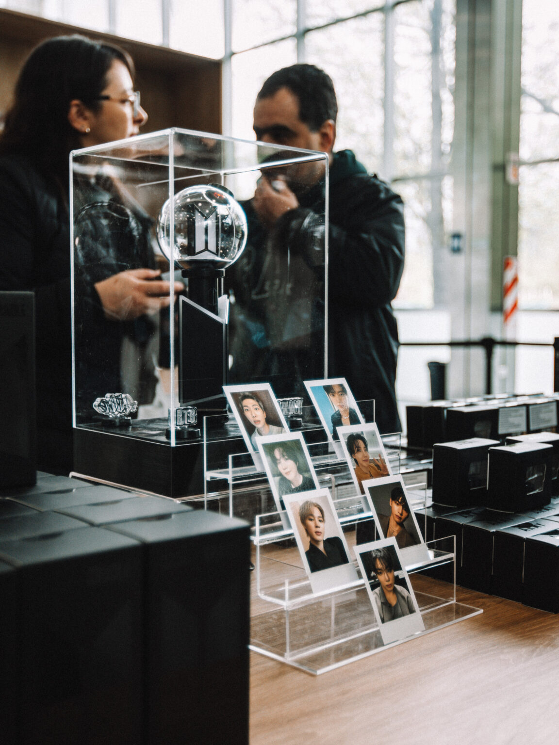Two visitors photographing the ARMY BOMB display case at the BTS POP-UP: ARIRANG IN BUENOS AIRES, Centro de Convenciones Dr. Arturo Frondizi, Vicente Lopez, 2026 — photographed by Anita Almaraz for K-HipHop Argentina