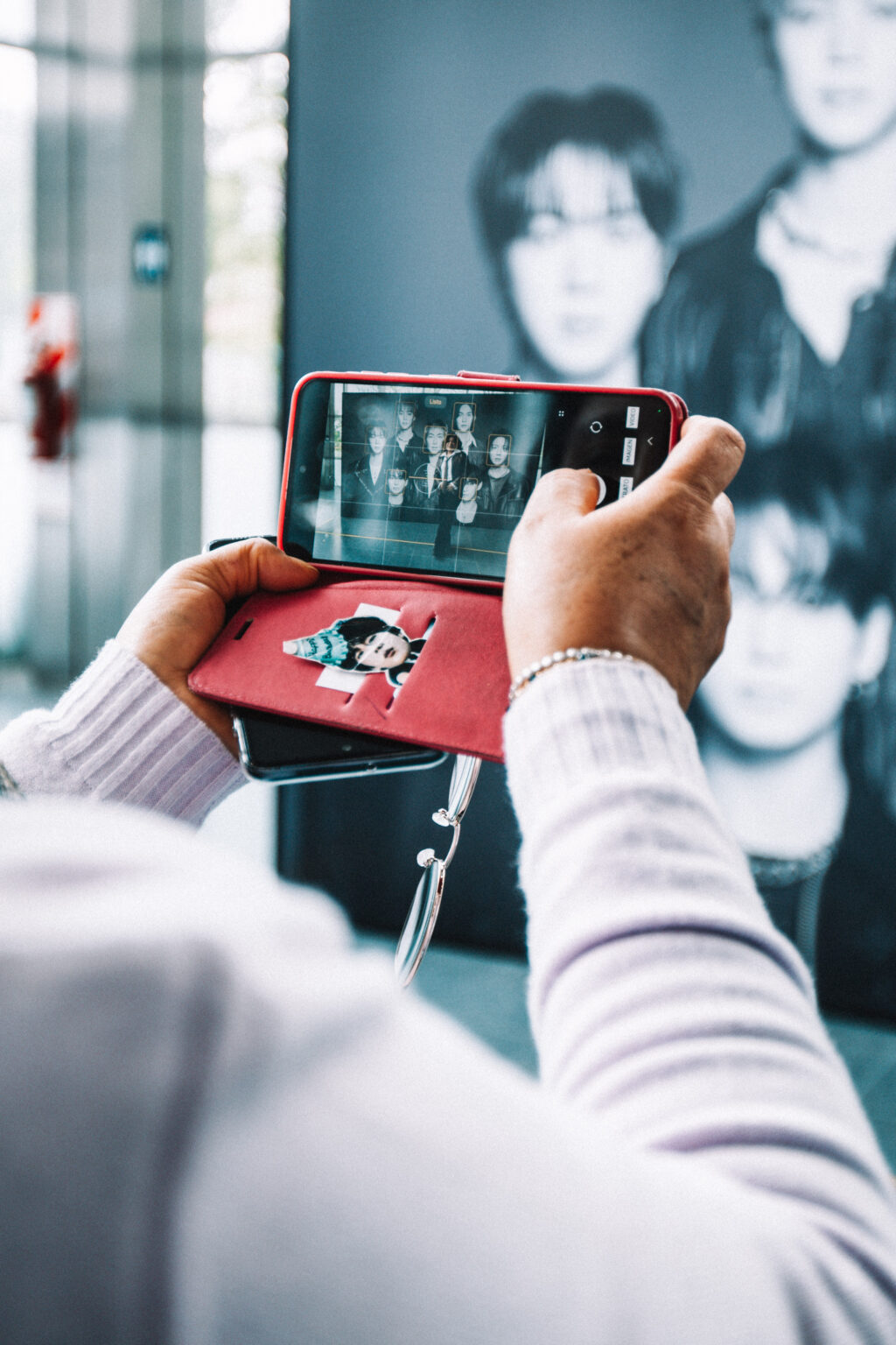 A visitor photographing a BTS portrait with her phone at the BTS POP-UP: ARIRANG IN BUENOS AIRES, Centro de Convenciones Dr. Arturo Frondizi, Vicente Lopez, 2026 — photographed by Anita Almaraz for K-HipHop Argentina