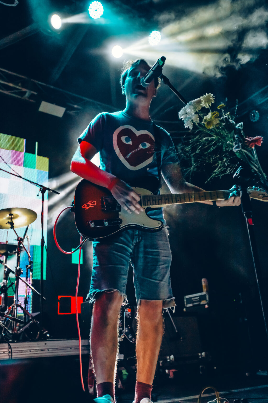 Seen from behind the amplifiers, a guitarist in a heart-printed T-shirt turning toward the drum kit &mdash; FestiLaptra at Ciudad Cultural Konex, Buenos Aires, 17 February 2024. Photographed by Anita Almaraz.