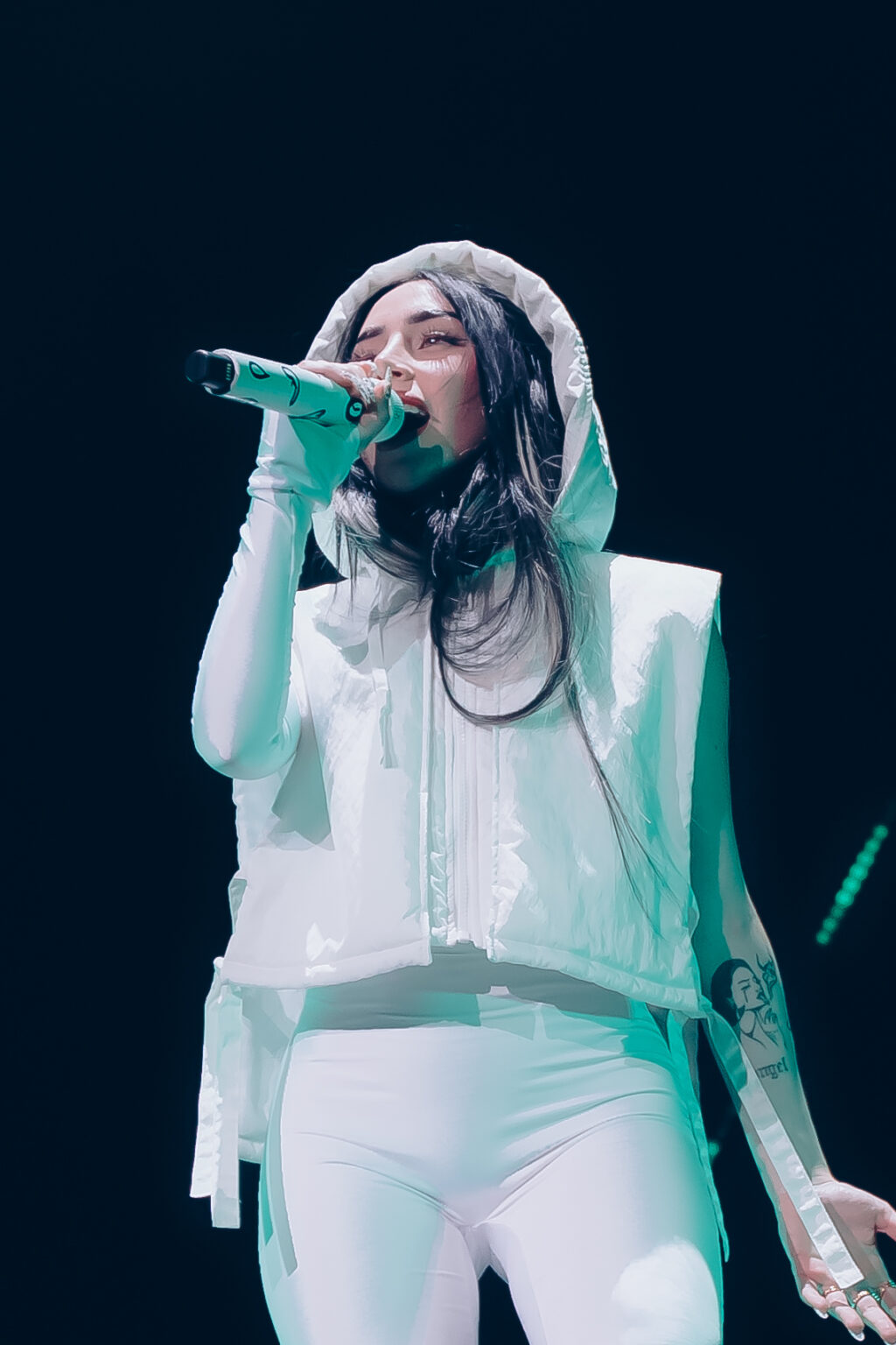 Close-up of Nicki Nicole singing into the microphone in a white hooded outfit — Movistar Arena, Buenos Aires, August 2023. Photographed by Anita Almaraz for Agencia Télam.