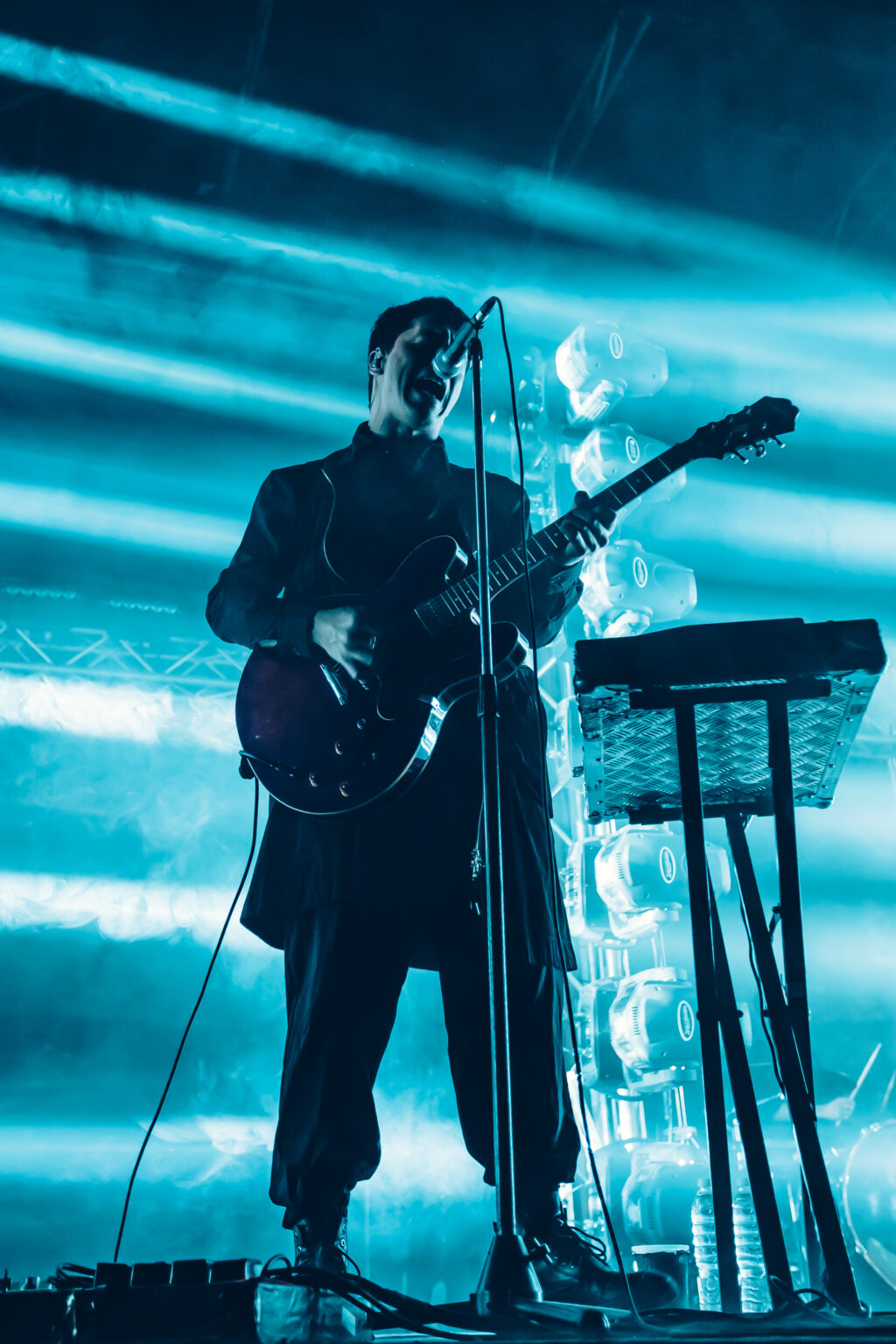 Guitarist in silhouette against blue beams beside the keyboards — Peces Raros at Estadio Obras Sanitarias, Buenos Aires, 7 October 2023. Photographed by Anita Almaraz.