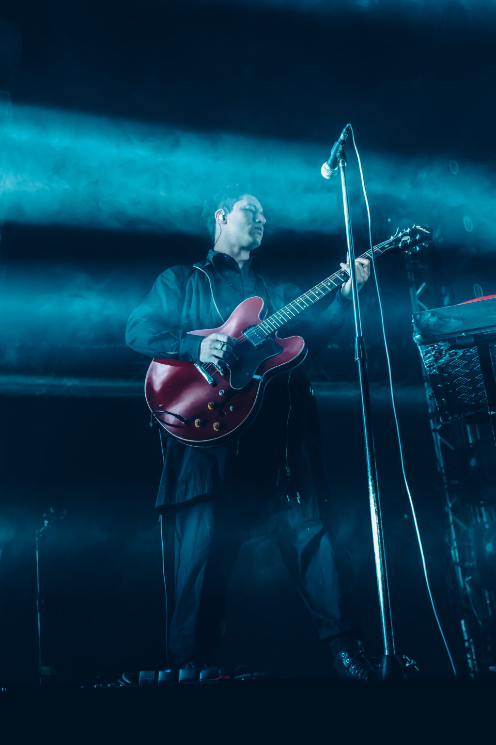 Guitarist lit in cold blue behind the microphone stand — Peces Raros at Estadio Obras Sanitarias, Buenos Aires, 7 October 2023. Photographed by Anita Almaraz.