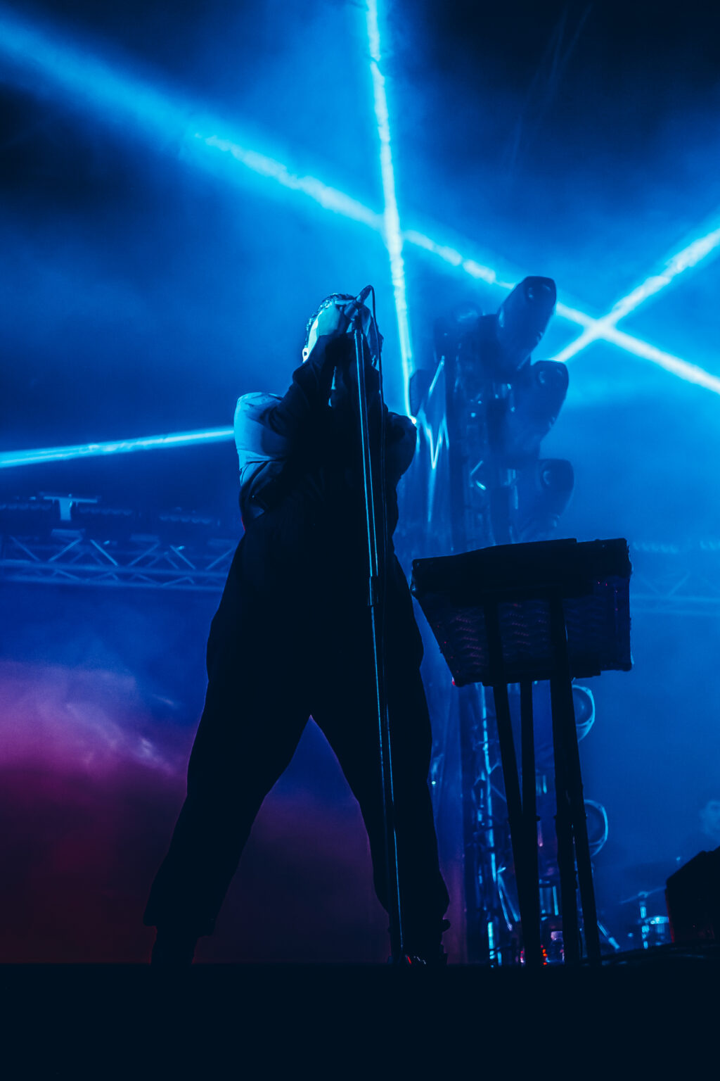 Singer in a long coat against crossing blue beams — Peces Raros at Estadio Obras Sanitarias, Buenos Aires, 7 October 2023. Photographed by Anita Almaraz.