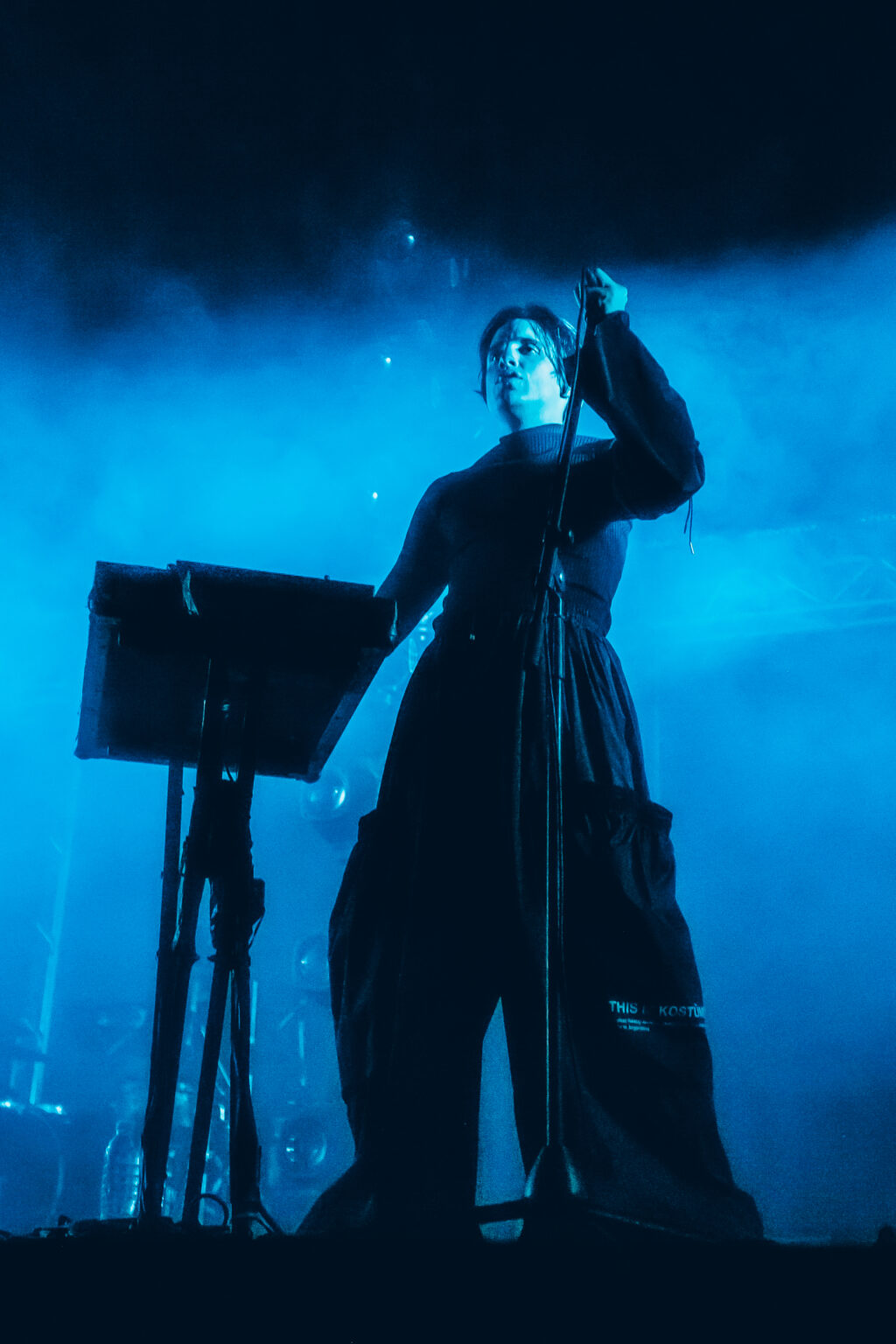 Singer with an arm raised in blue light — Peces Raros at Estadio Obras Sanitarias, Buenos Aires, 7 October 2023. Photographed by Anita Almaraz.