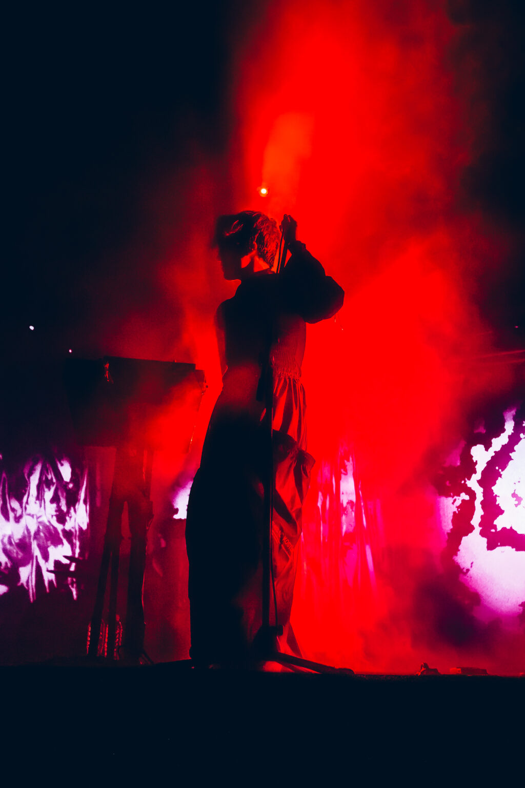 Singer in silhouette with hands to the head in red light — Peces Raros at Estadio Obras Sanitarias, Buenos Aires, 7 October 2023. Photographed by Anita Almaraz.