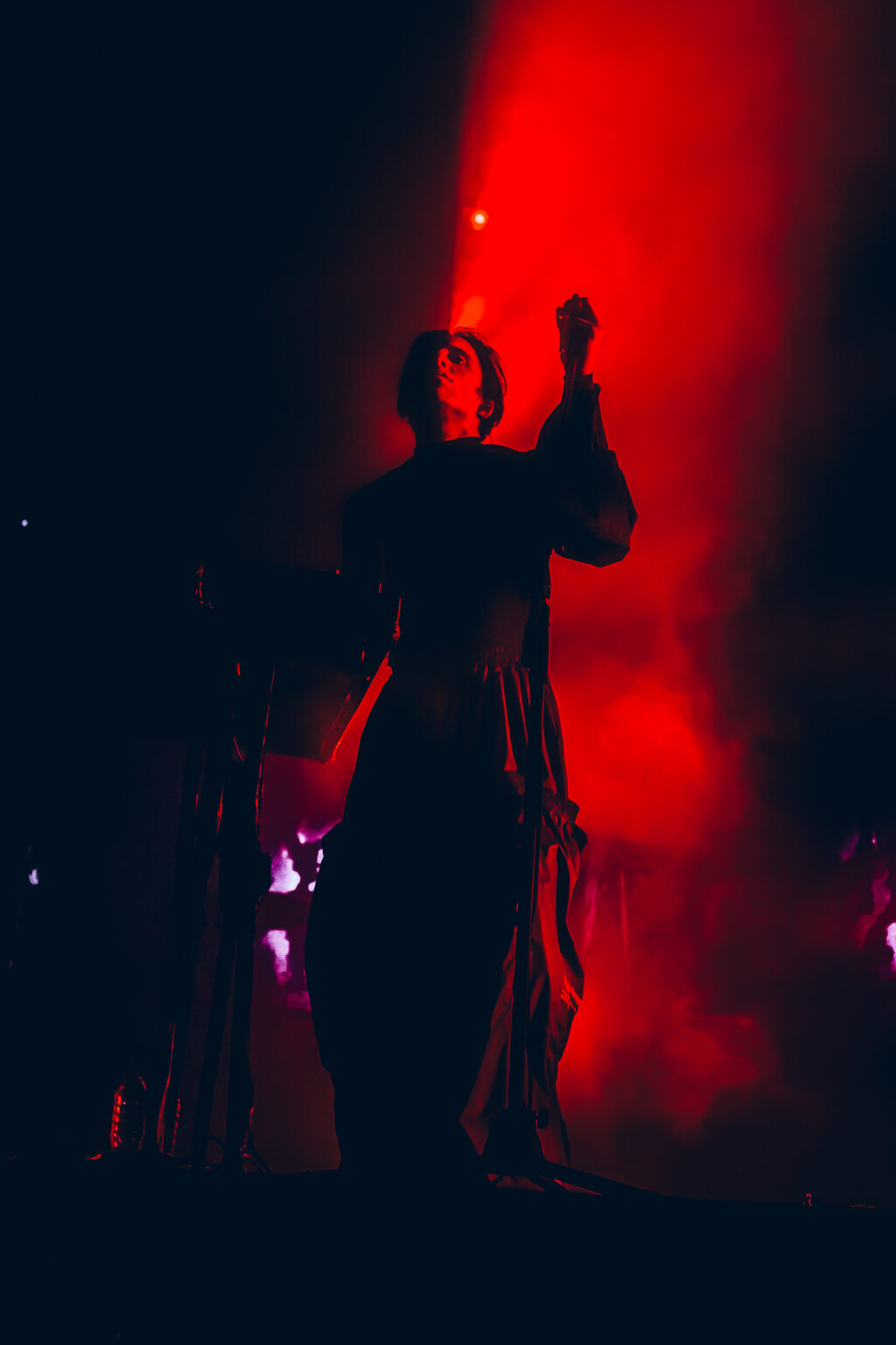 Singer with an arm raised in red light — Peces Raros at Estadio Obras Sanitarias, Buenos Aires, 7 October 2023. Photographed by Anita Almaraz.