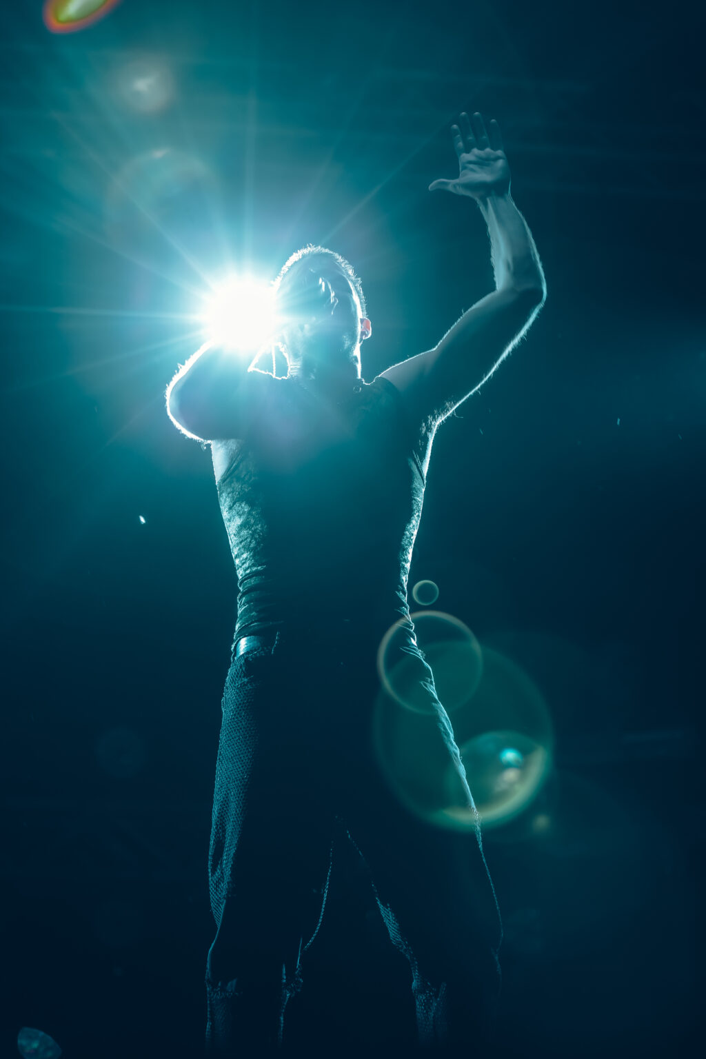 Wos backlit by a spotlight, microphone raised — Wos live in Buenos Aires, photographed by Anita Almaraz.