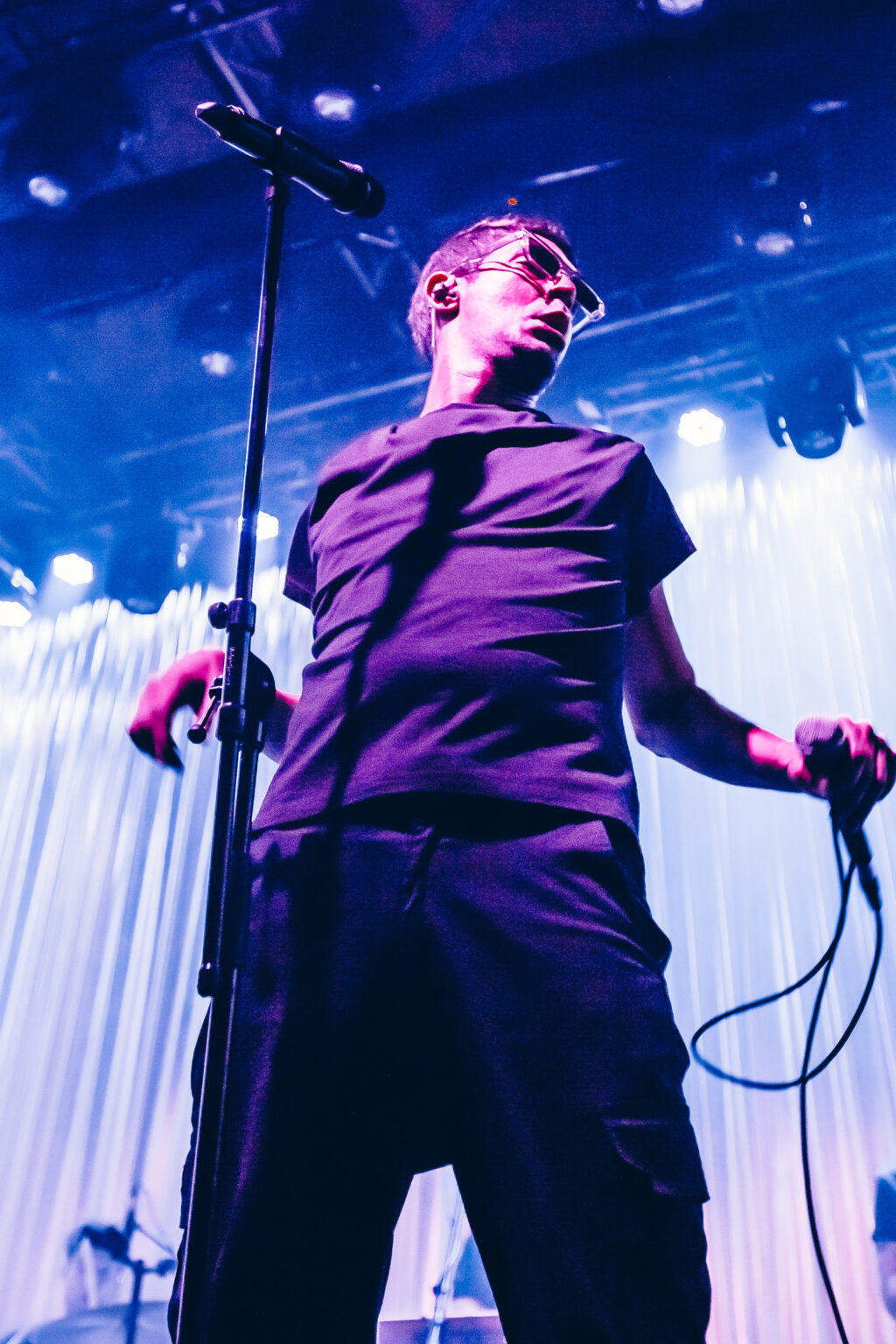 Singer with the cable in hand under blue light — El Kuelgue at C Complejo Art Media, Buenos Aires, 23 November 2023. Photographed by Anita Almaraz.