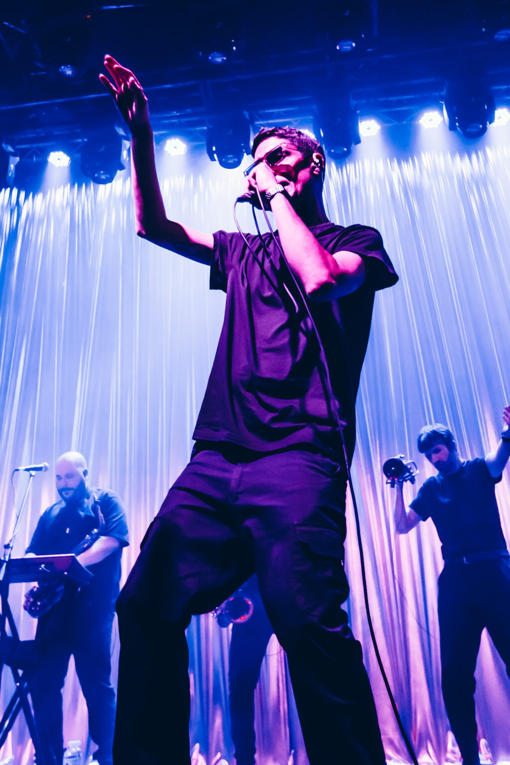 Singer with an arm raised under blue beams — El Kuelgue at C Complejo Art Media, Buenos Aires, 23 November 2023. Photographed by Anita Almaraz.