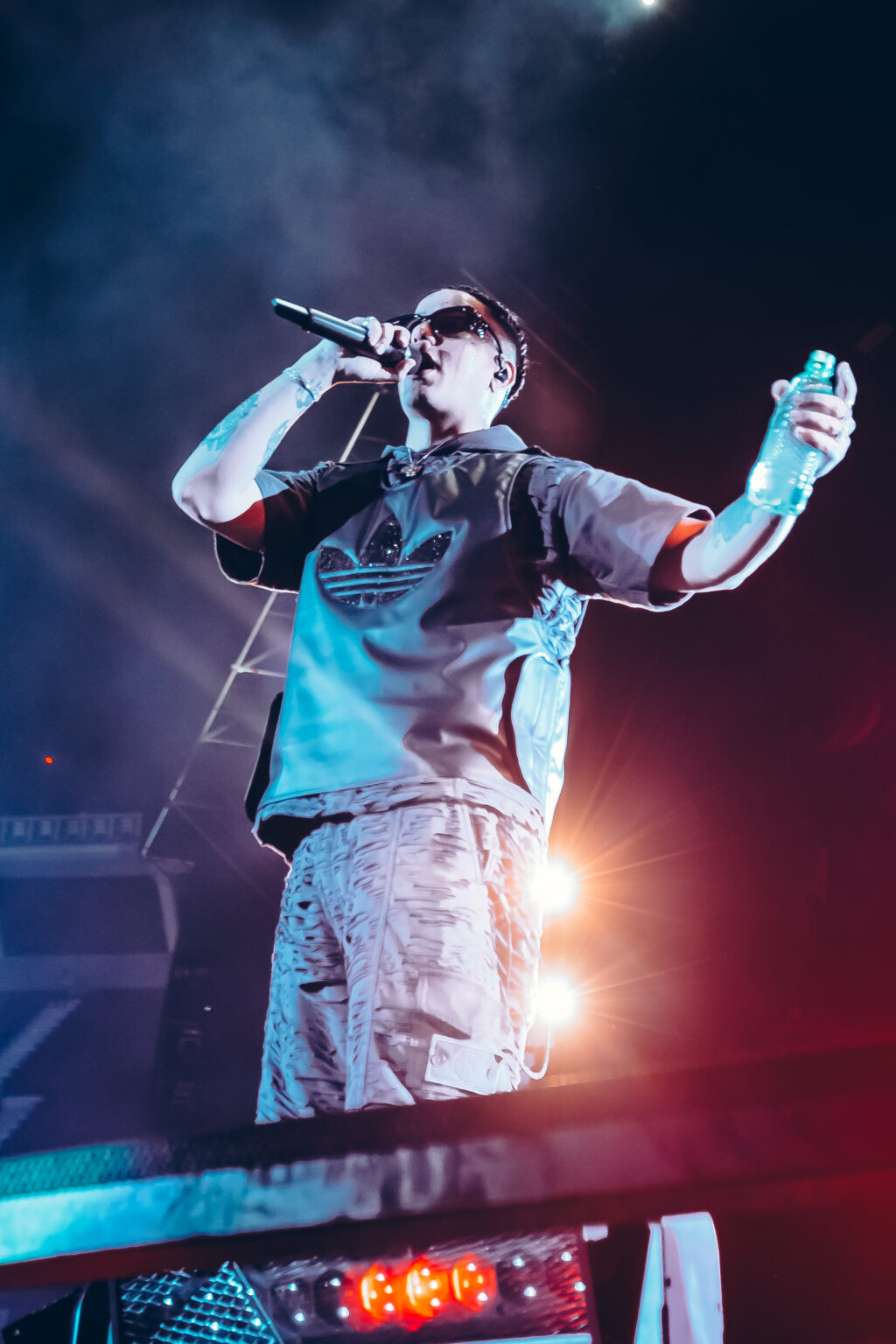 Duki singing into the microphone, lit in blue and orange — Duki at Estadio River Plate, Buenos Aires, 2 December 2023. Photographed by Anita Almaraz.