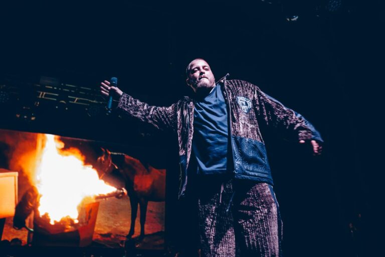 The artist with his arms out beside a burst of flame — Zeballos presenting Asimetría at Vorterix, Buenos Aires, 2026. Photographed by Anita Almaraz.