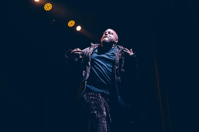 The artist with his arms out in blue light — Zeballos presenting Asimetría at Vorterix, Buenos Aires, 2026. Photographed by Anita Almaraz.