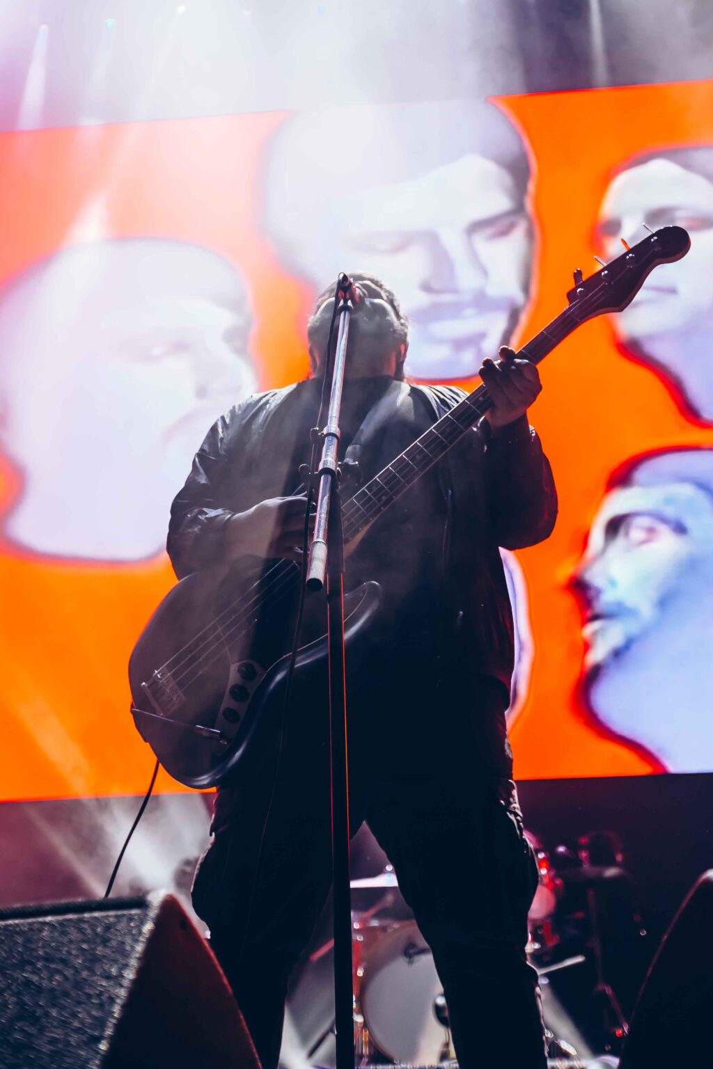 Singer in silhouette against the screen of painted faces — El Mató a un Policía Motorizado at Movistar Arena, Buenos Aires, 16 June 2024. Photographed by Anita Almaraz.