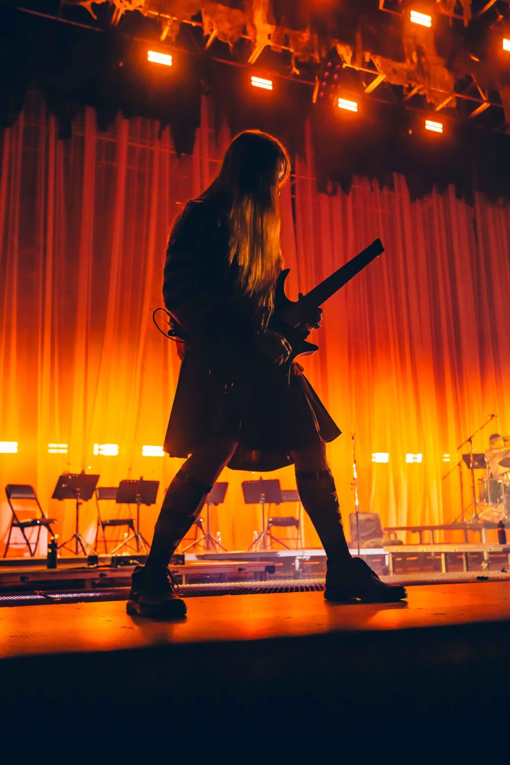 A figure in silhouette with a guitar against the orange curtain — Dillom at Estadio Luna Park, Buenos Aires, 19 June 2024. Photographed by Anita Almaraz.
